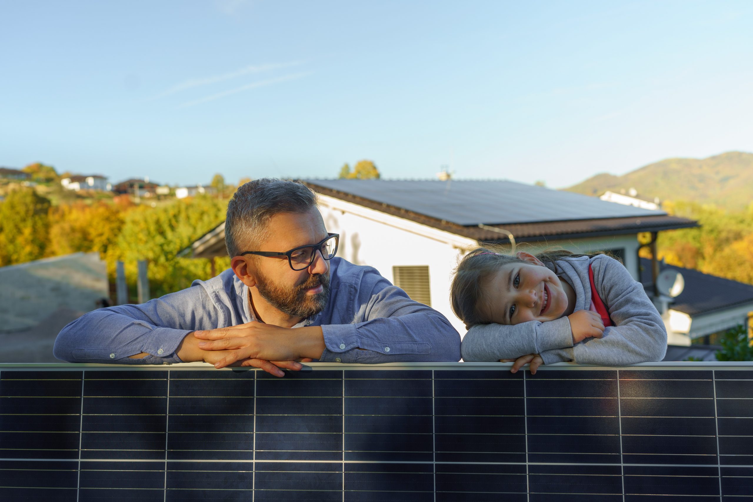 Father with his little daughter near their house with solar panels. Alternative energy, saving resources and sustainable lifestyle concept.