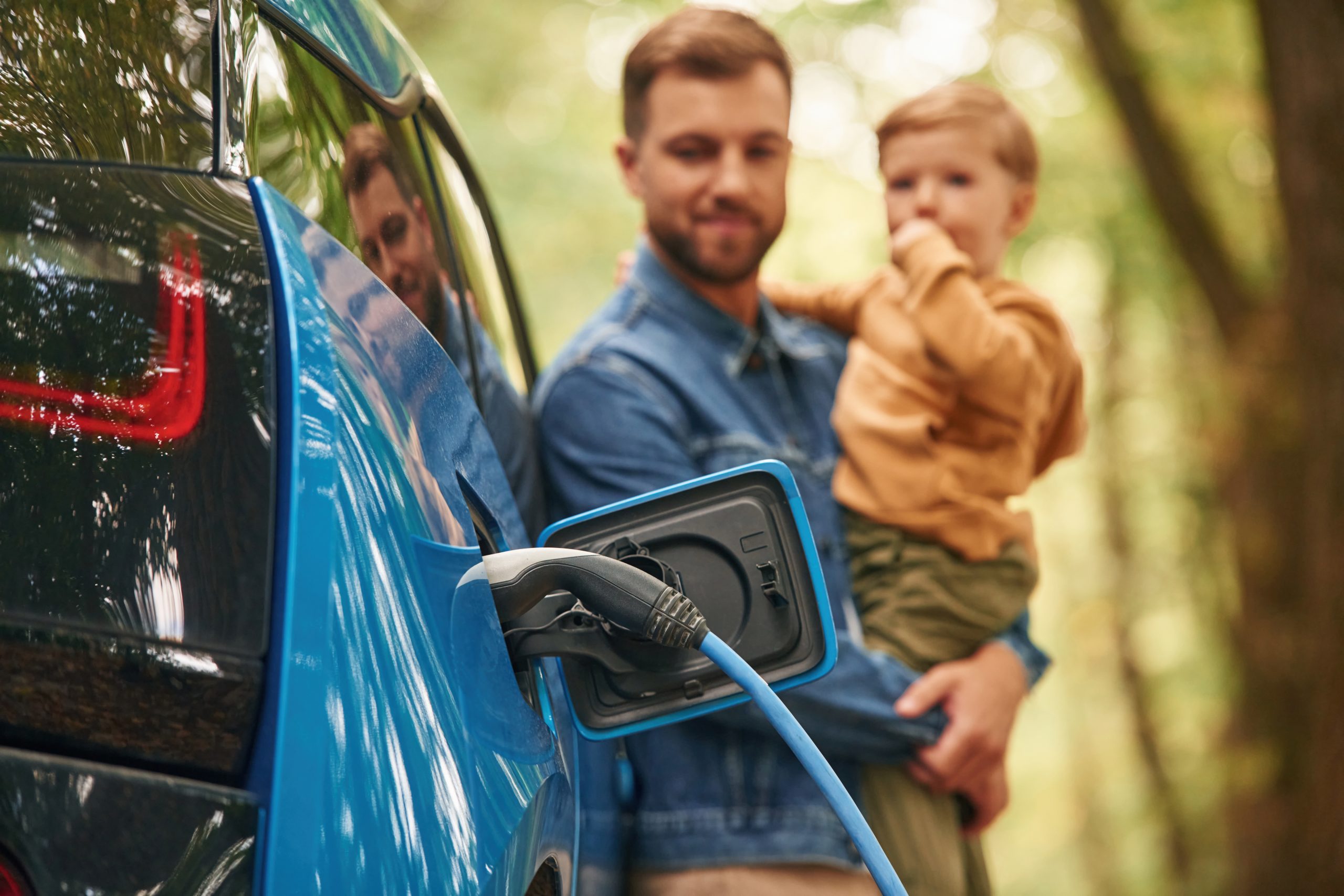 Close up view of wire in the socket. Father with his little son are waiting for electric car to charge